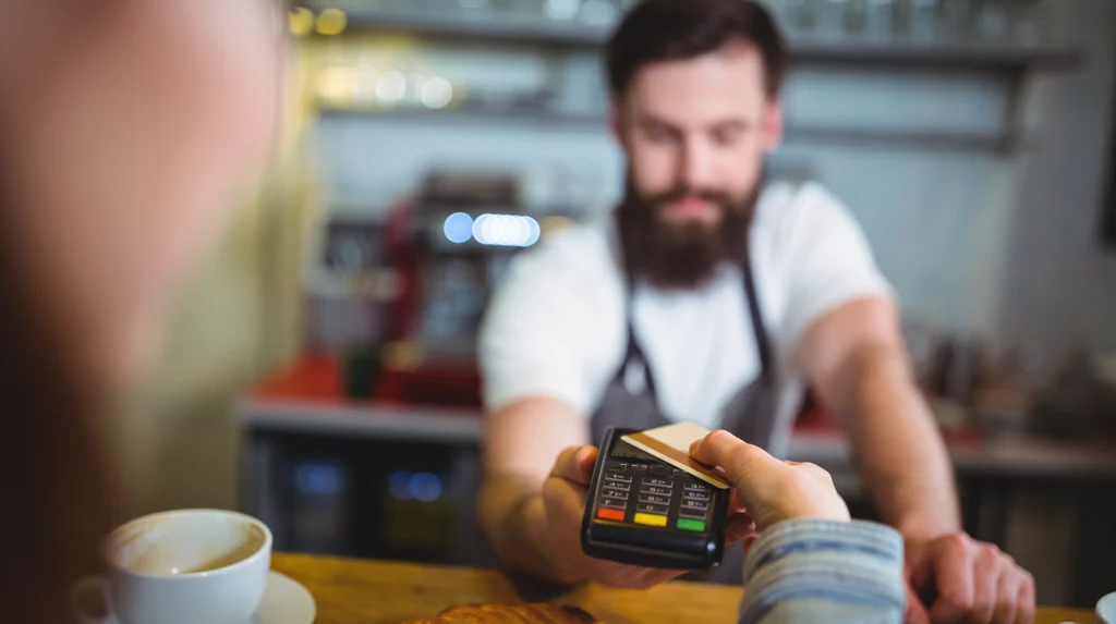 Customer pays a restaurant server with a card terminal at the counter.