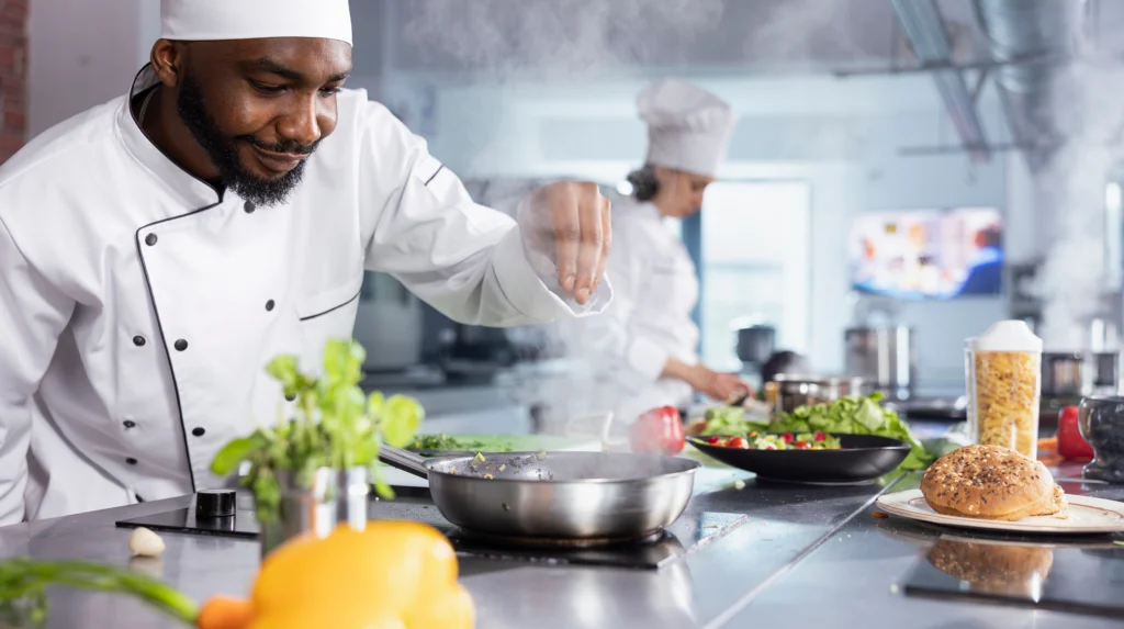Chef seasoning food at the stove in a commercial kitchen