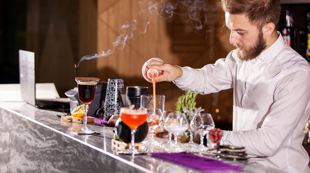 Bartender pouring a pink cocktail mixture behind a restaurant bar