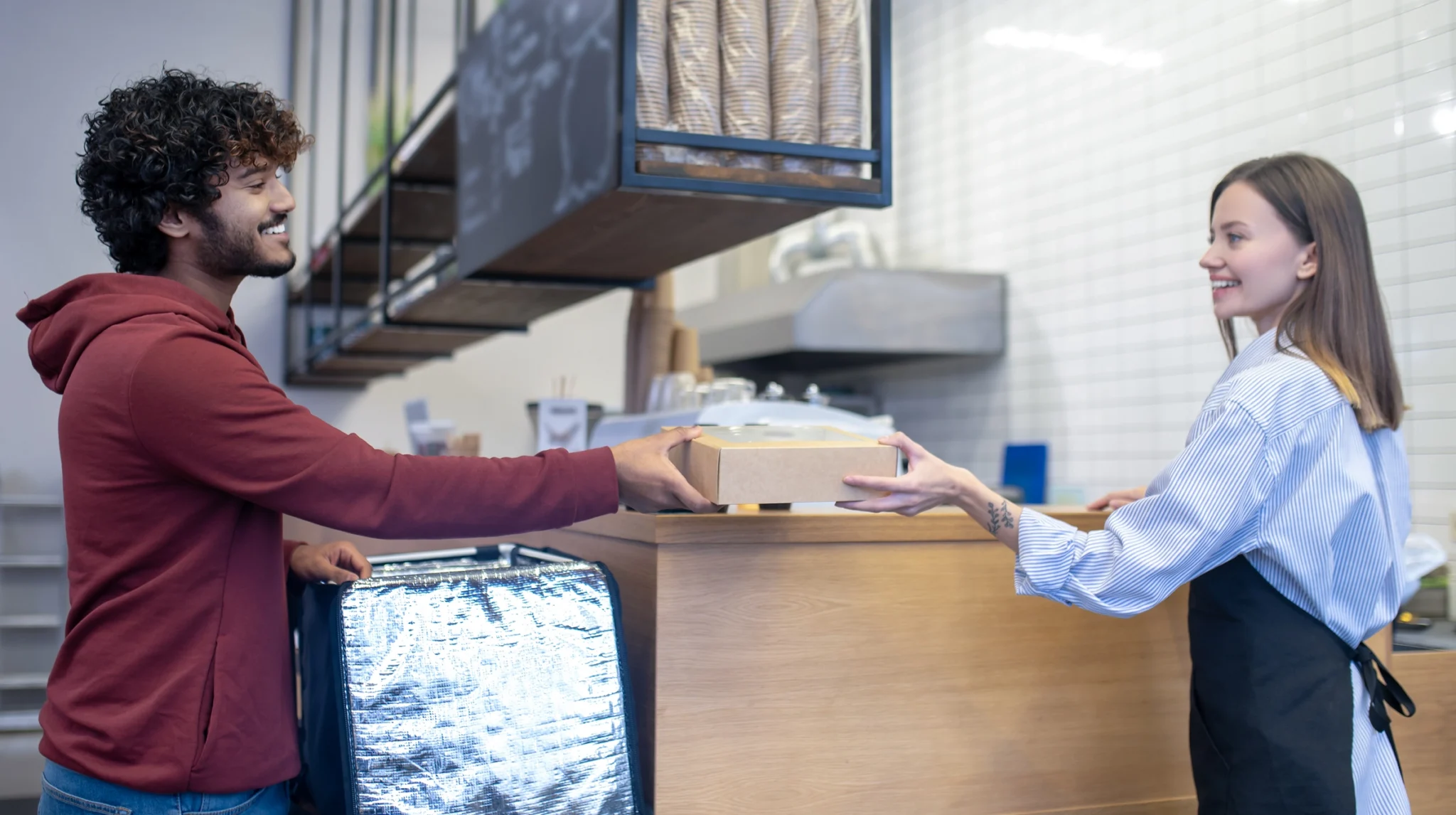 Restaurant employee passing a packaged takeout food container to a delivery courier.