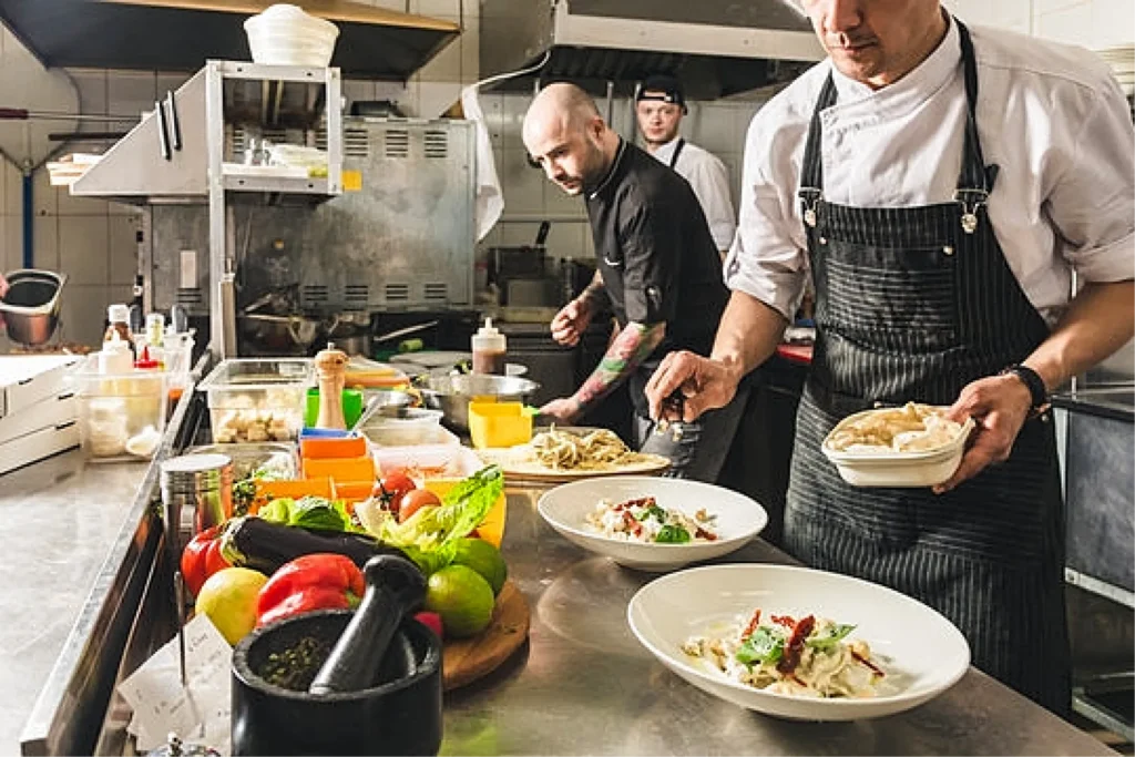 Professional chefs preparing and plating meals on a commercial kitchen line.
