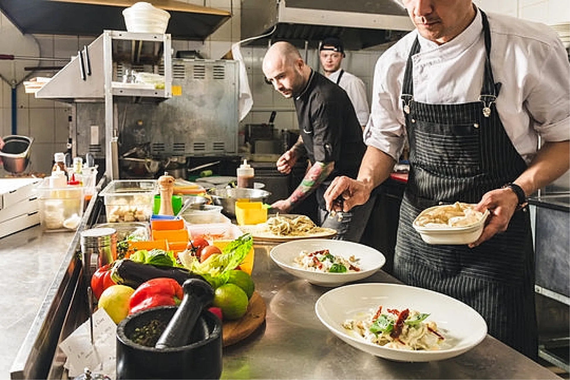 Professional chefs preparing and plating meals on a commercial kitchen line.