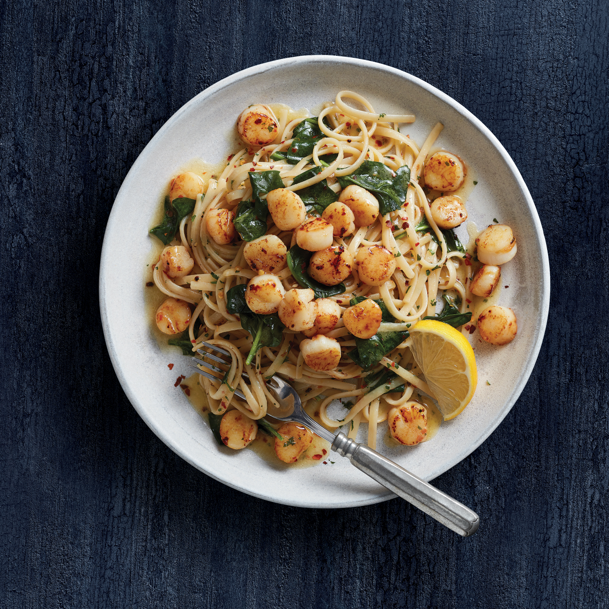 Slade Gorton scallops served over pasta with spinach and lemon in a white bowl
